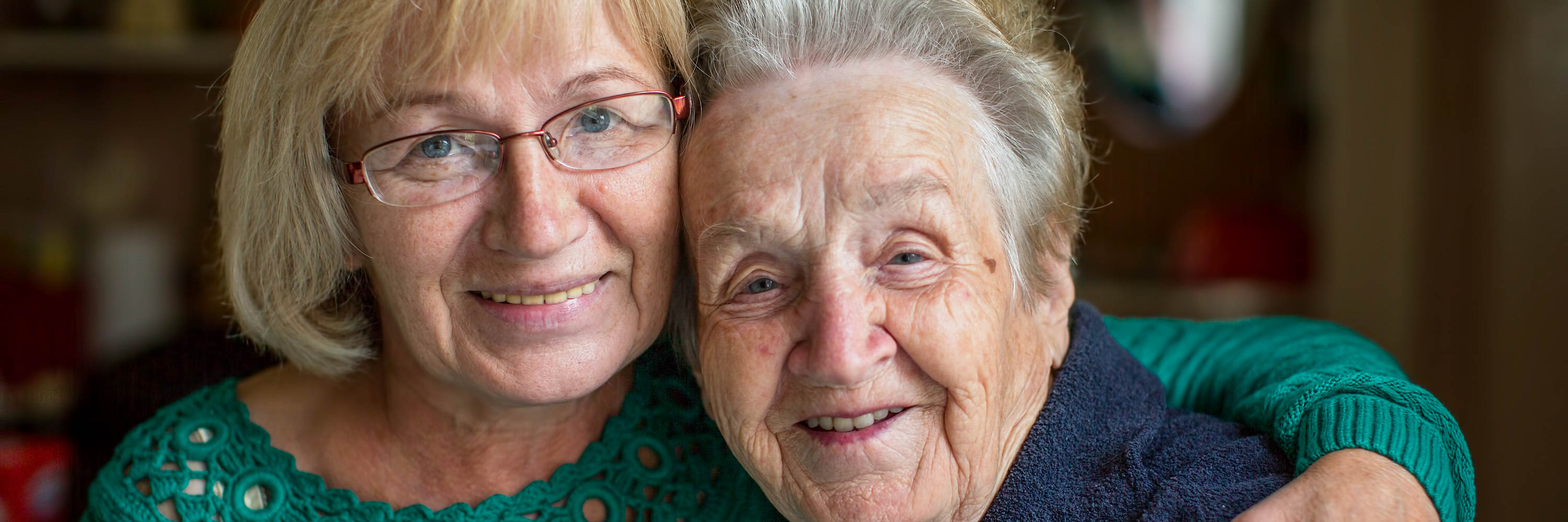Close-up portrait of a mature women with glasses holding a senior women as they both smile.